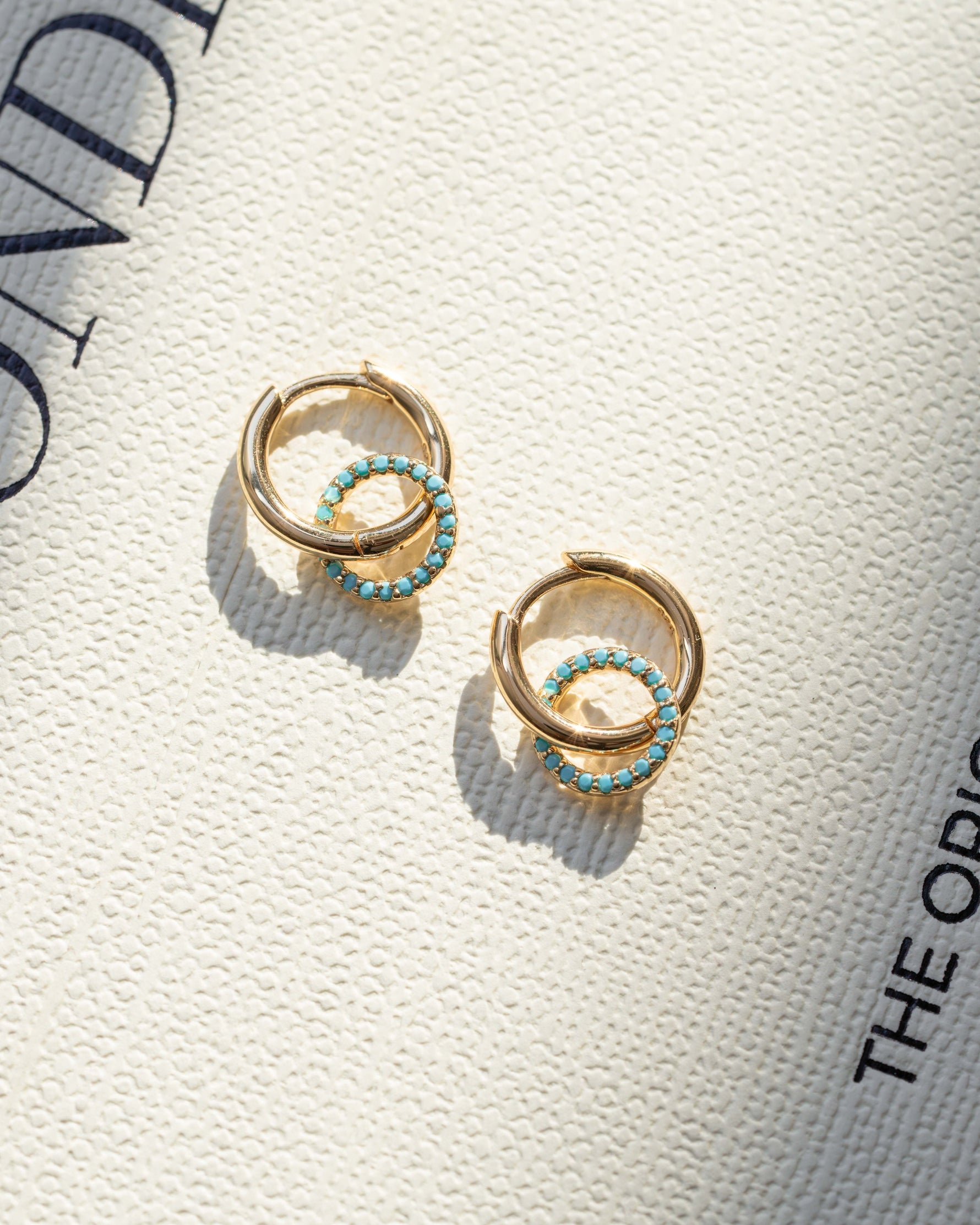 gold dangle earrings with turquoise charms laying on a fashion book