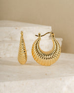 Gold statement earrings featuring a thick hoop earring and a neutral background