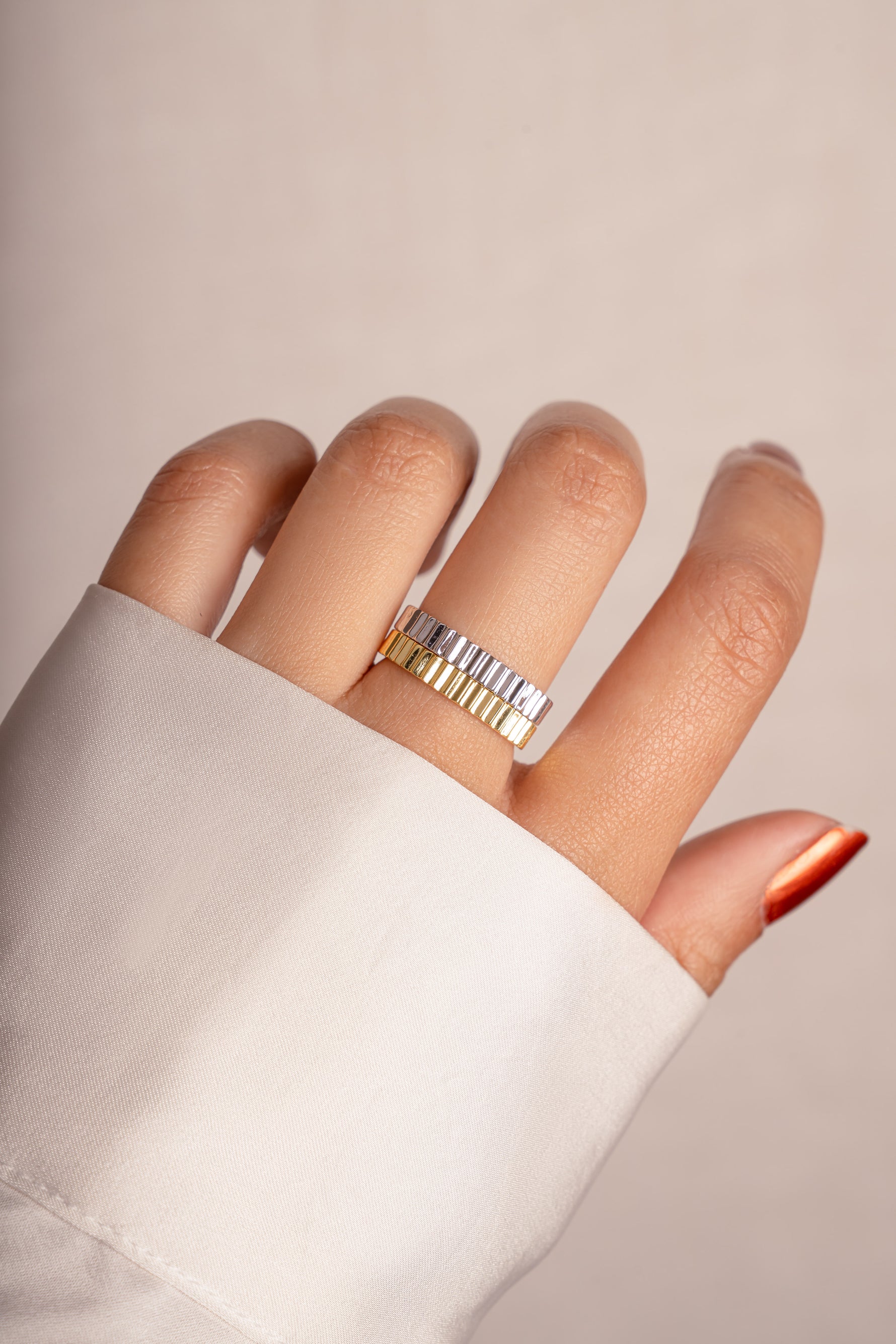 Model wearing stacked gold and silver ridged textured rings. 