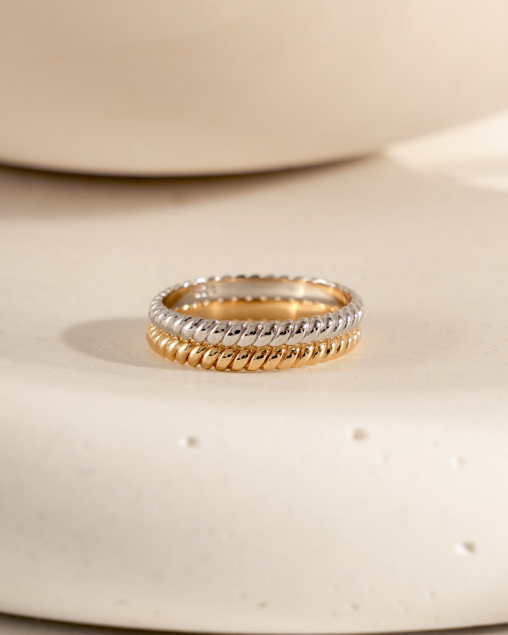 Gold ring with a textured band, and sterling silver stacking rope ring on a white ceramic surface