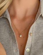 Everyday necklace with a gold chain and diamond pendant worn by a person in a gray ribbed shirt.