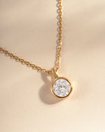 Gold necklace with a round diamond pendant on a beige background