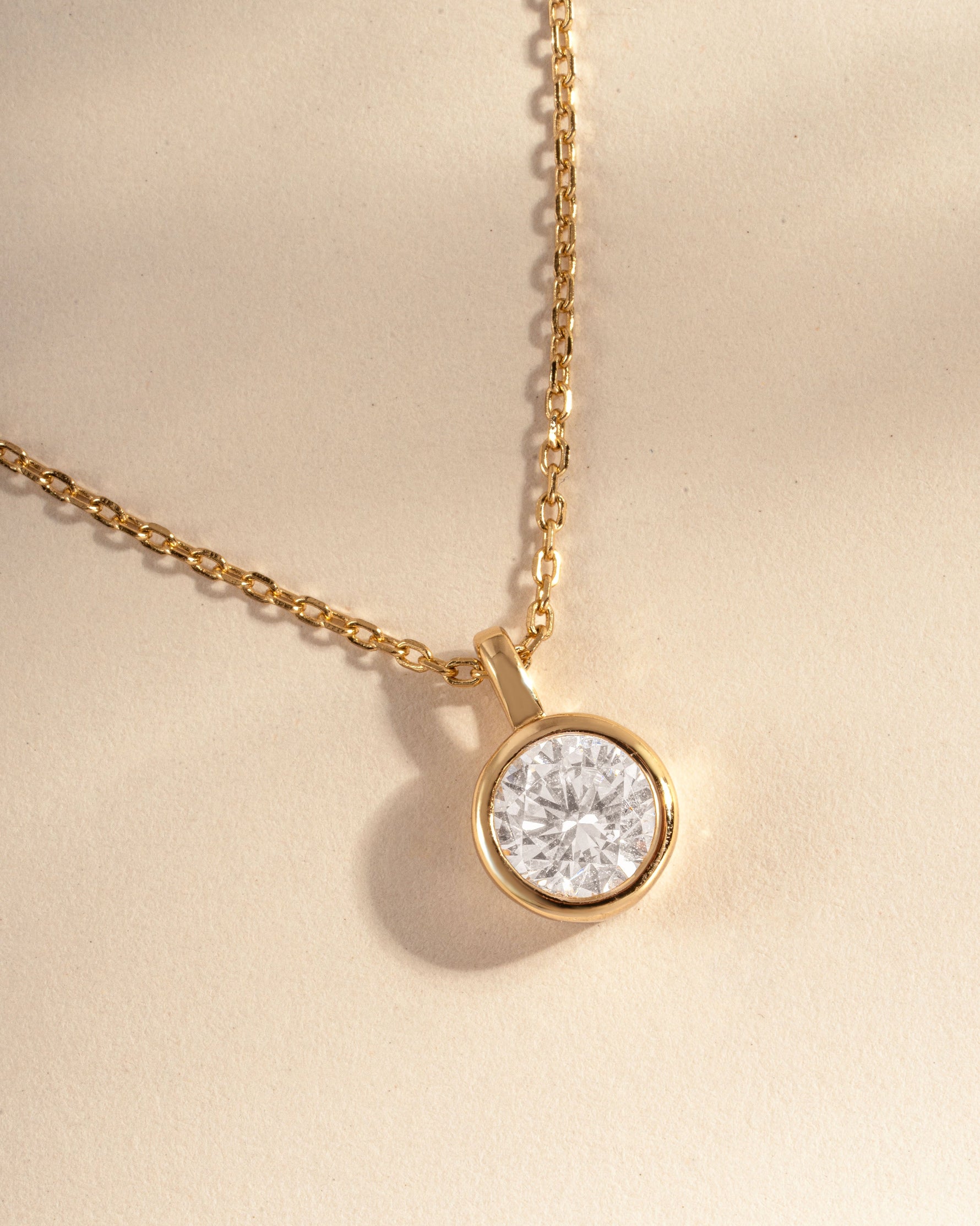 Gold necklace with a round diamond pendant on a beige background