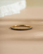 Gold diamond eternity ring with a sapphire september birthstone on a beige surface