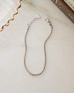 Silver adjustable bracelet with a thin chain on a marble surface