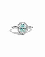 Silver ring with a aquamarine gemstone and diamond-studded halo on a white background
