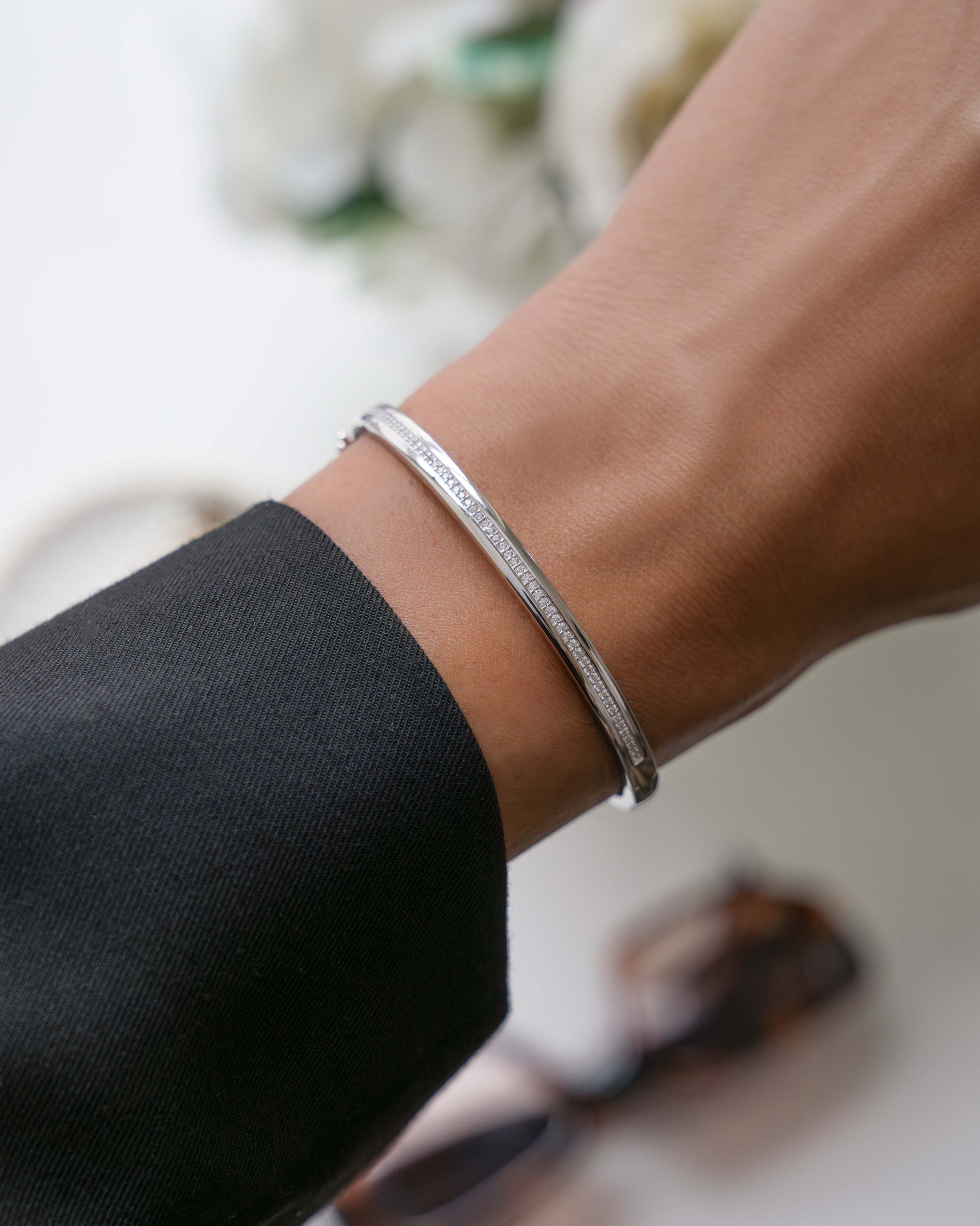 Sterling silver bridesmaids jewelry featuring a silver bangle bracelet with cz stones on a models wrist with a blurred background