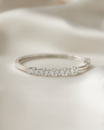 Silver bangle with multiple small cubic zirconia diamonds on a beige fabric background