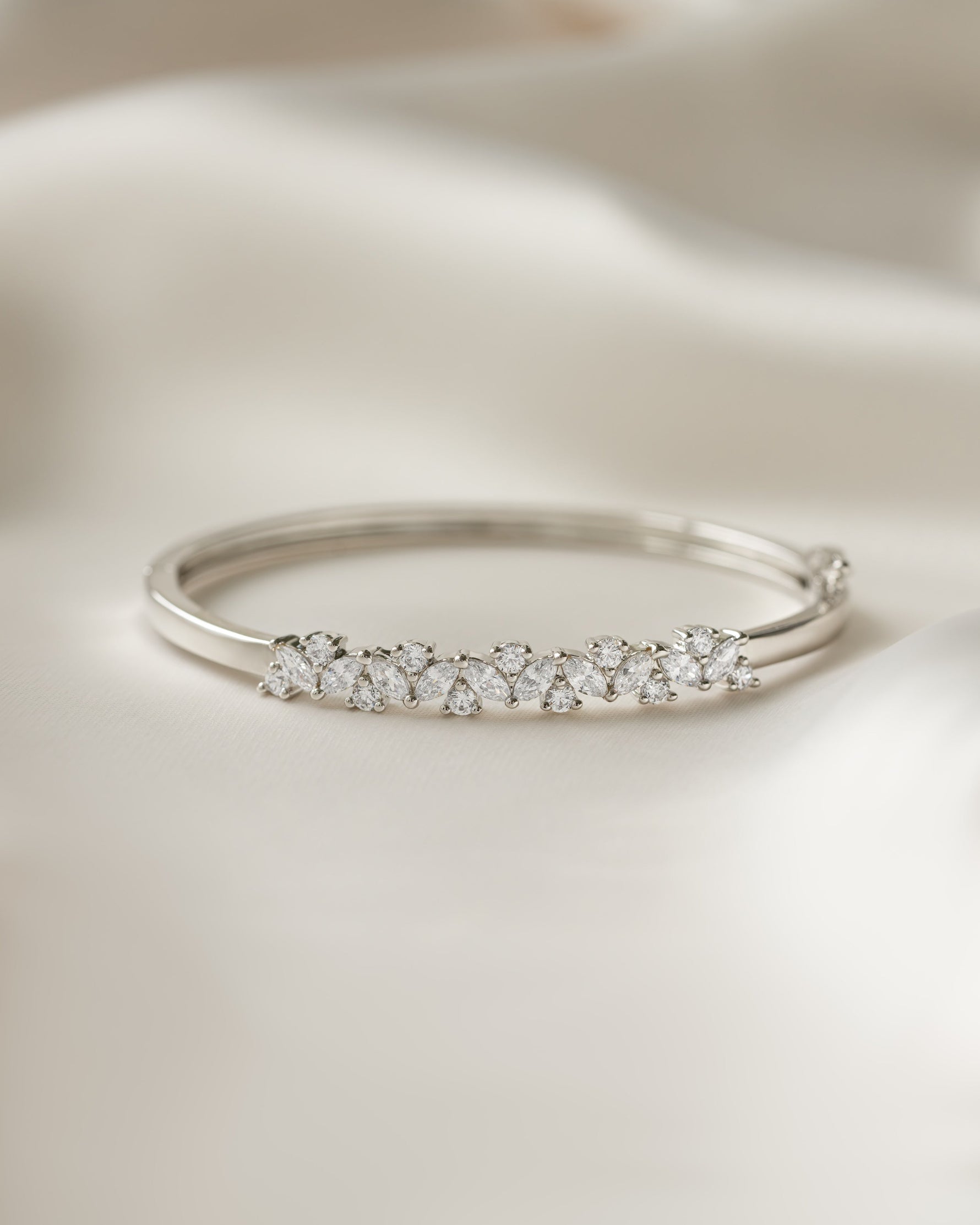 Silver bangle with multiple small cubic zirconia diamonds on a beige fabric background