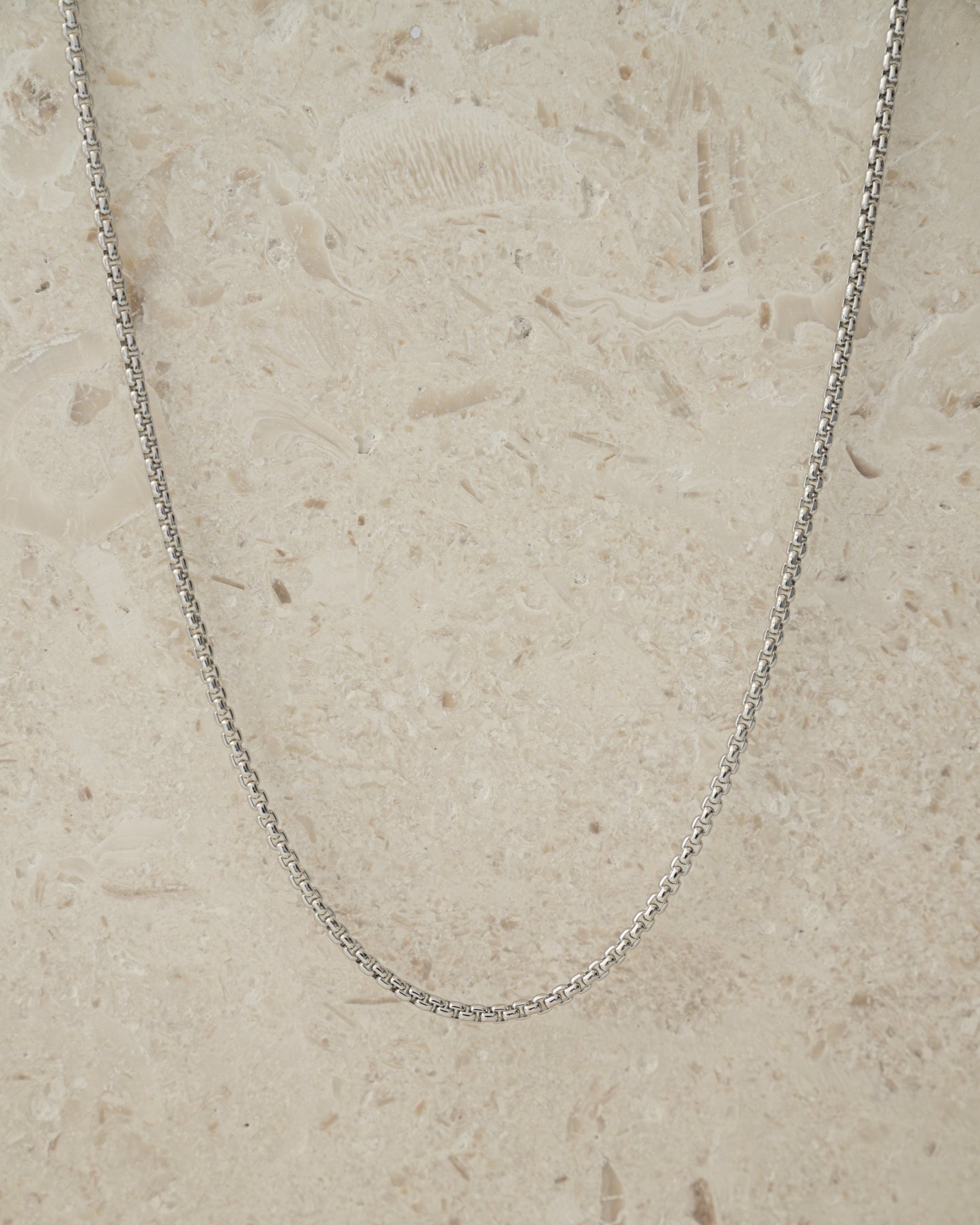 Silver box chain necklace on a beige background