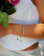 model holding flowers wearing a silver chain link bracelet, a two-tone round bezel tennis bracelet, and a dainty cubic zirconia tennis bracelet 