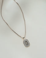 Closeup image of silver chain initial necklace on plain background