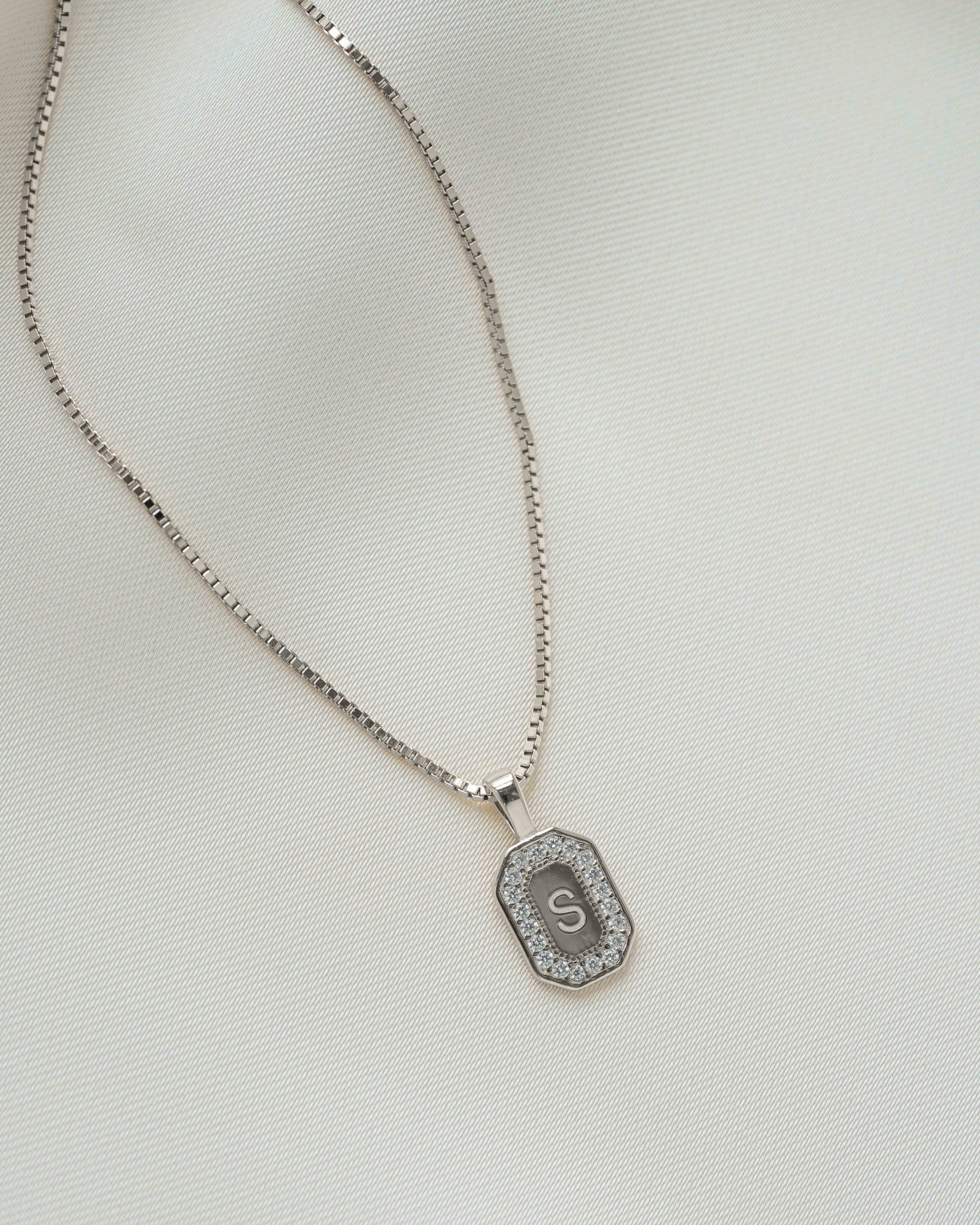 Closeup image of silver chain initial necklace on plain background