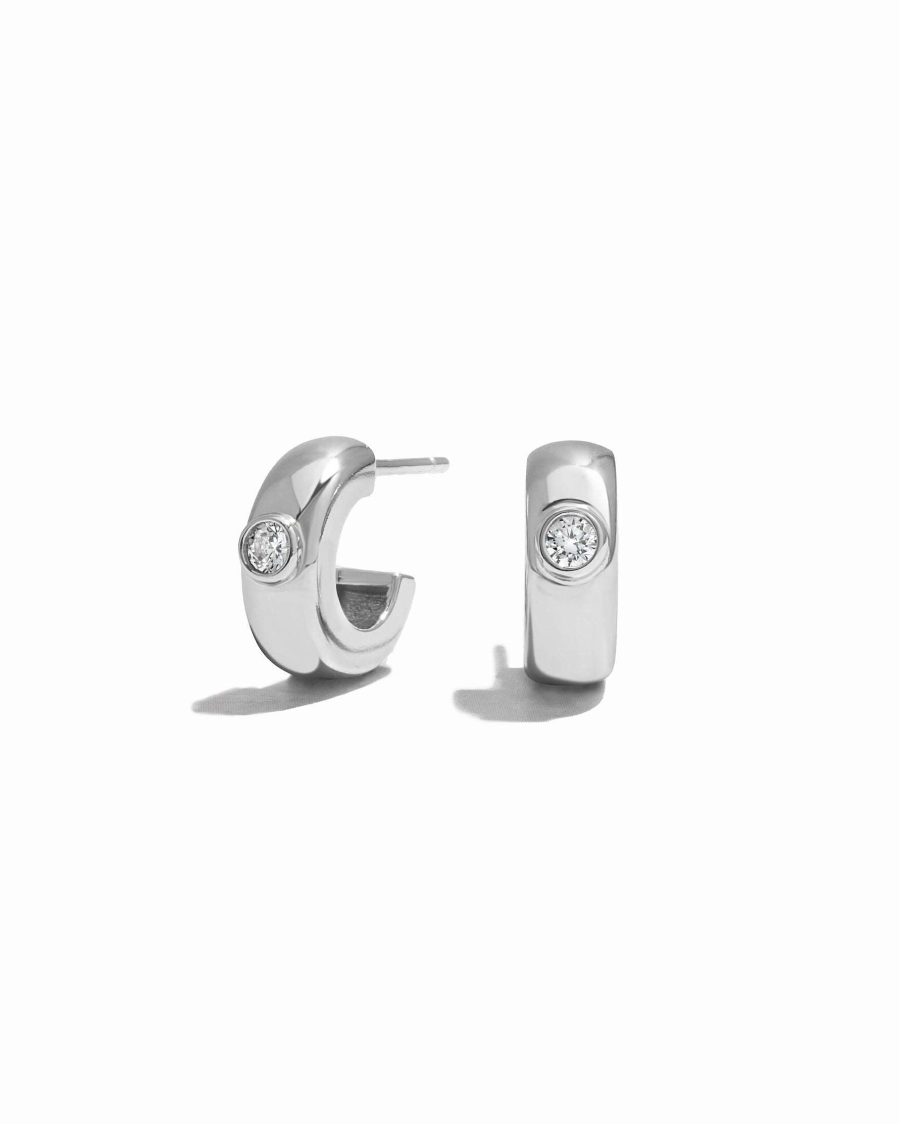Pair of silver small hoop earrings earrings with a white cubic zirconia stone on a white background