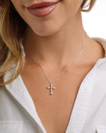 Close-up of a model wearing a silver chain cross necklace with a white background