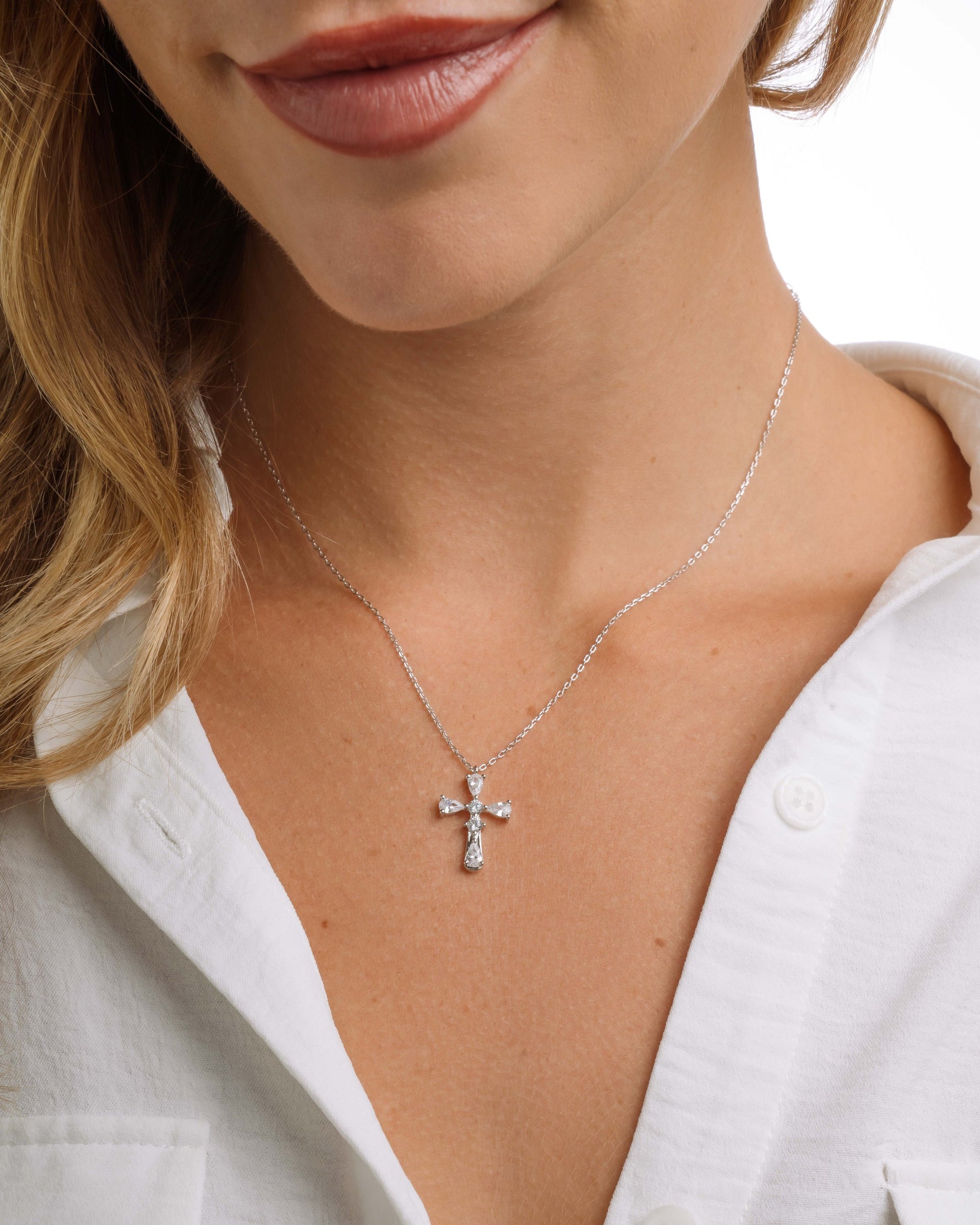 Close-up of a model wearing a silver chain cross necklace with a white background