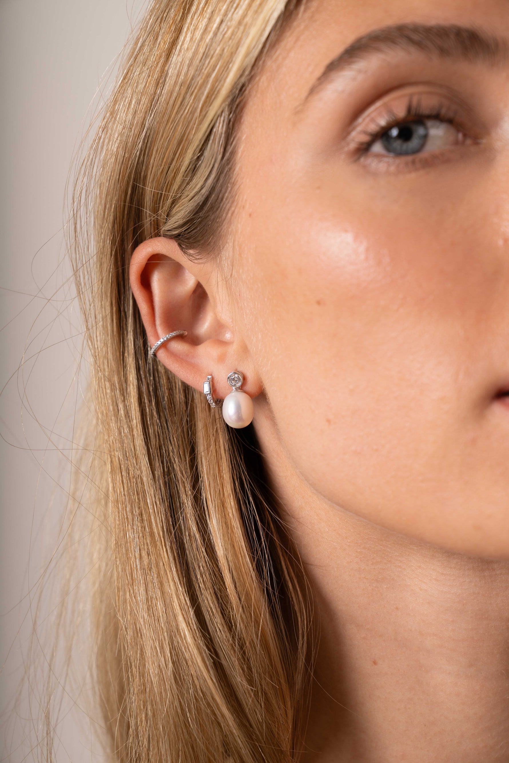 Model wearing a silver diamond ear cuff, a baguette huggie hoop, and a pearl drop earring