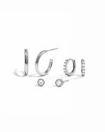 Silver hoop earrings, diamond huggies, and diamond bezel set studs on a white background