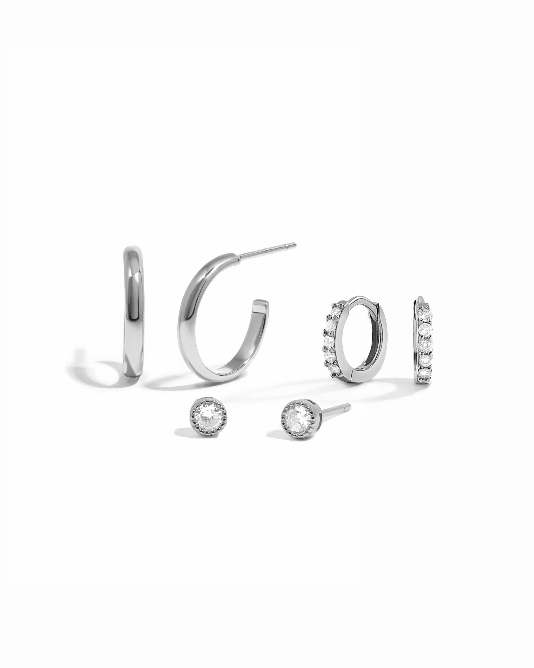 Silver hoop earrings, diamond huggies, and diamond bezel set studs on a white background