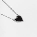 Close-up of a silver necklace with a black heart pendant with a black stone and pave diamond details
