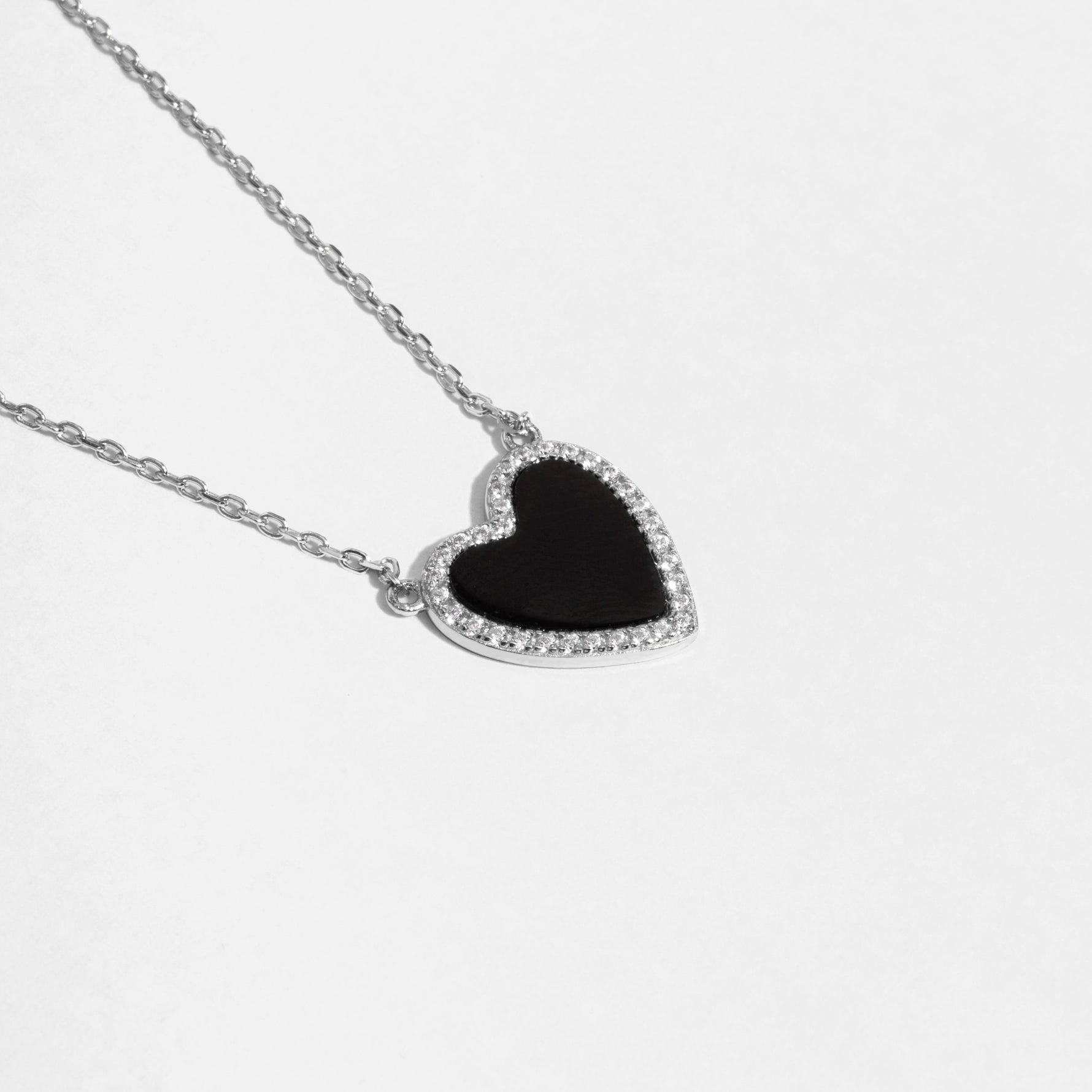 Close-up of a silver necklace with a black heart pendant with a black stone and pave diamond details
