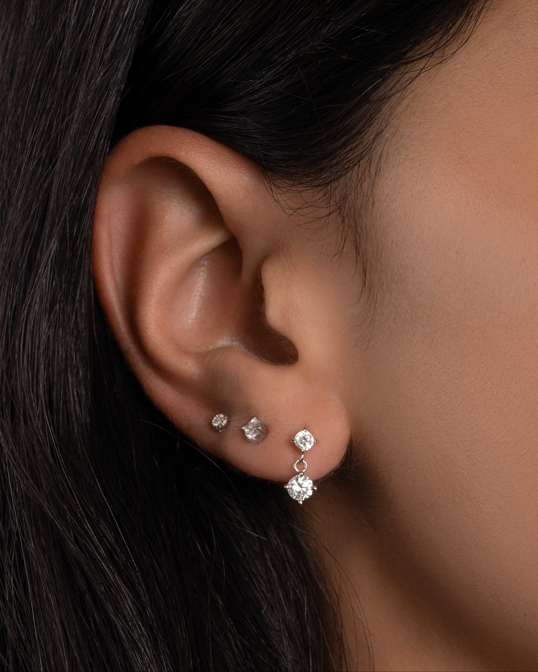 Model wearing sterling silver dainty earrings featuring a diamond charm earring and dainty diamond studs 