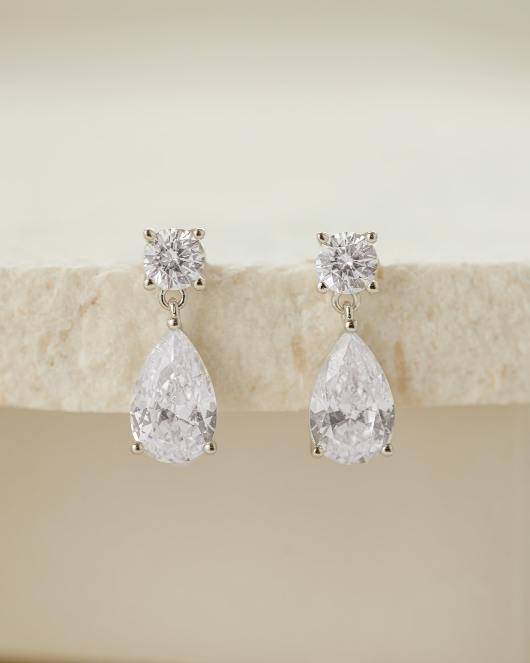 Sterling silver teardrop-shaped diamond earrings on a beige stone surface