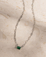 Silver chaing gemstone necklace with a green gemstone on a beige stone surface