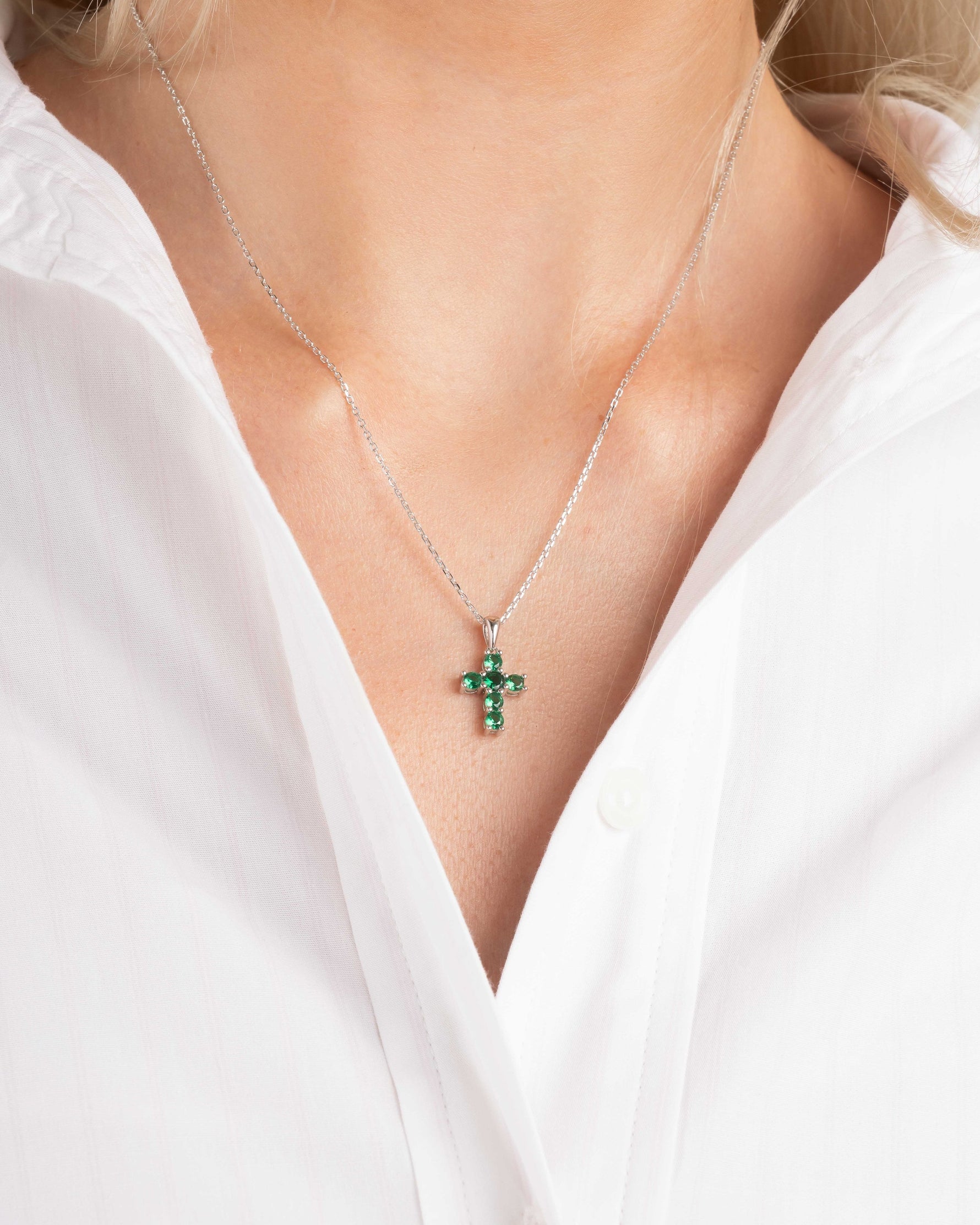 Model wearing religious jewelry featuring and emerald green cross pendant