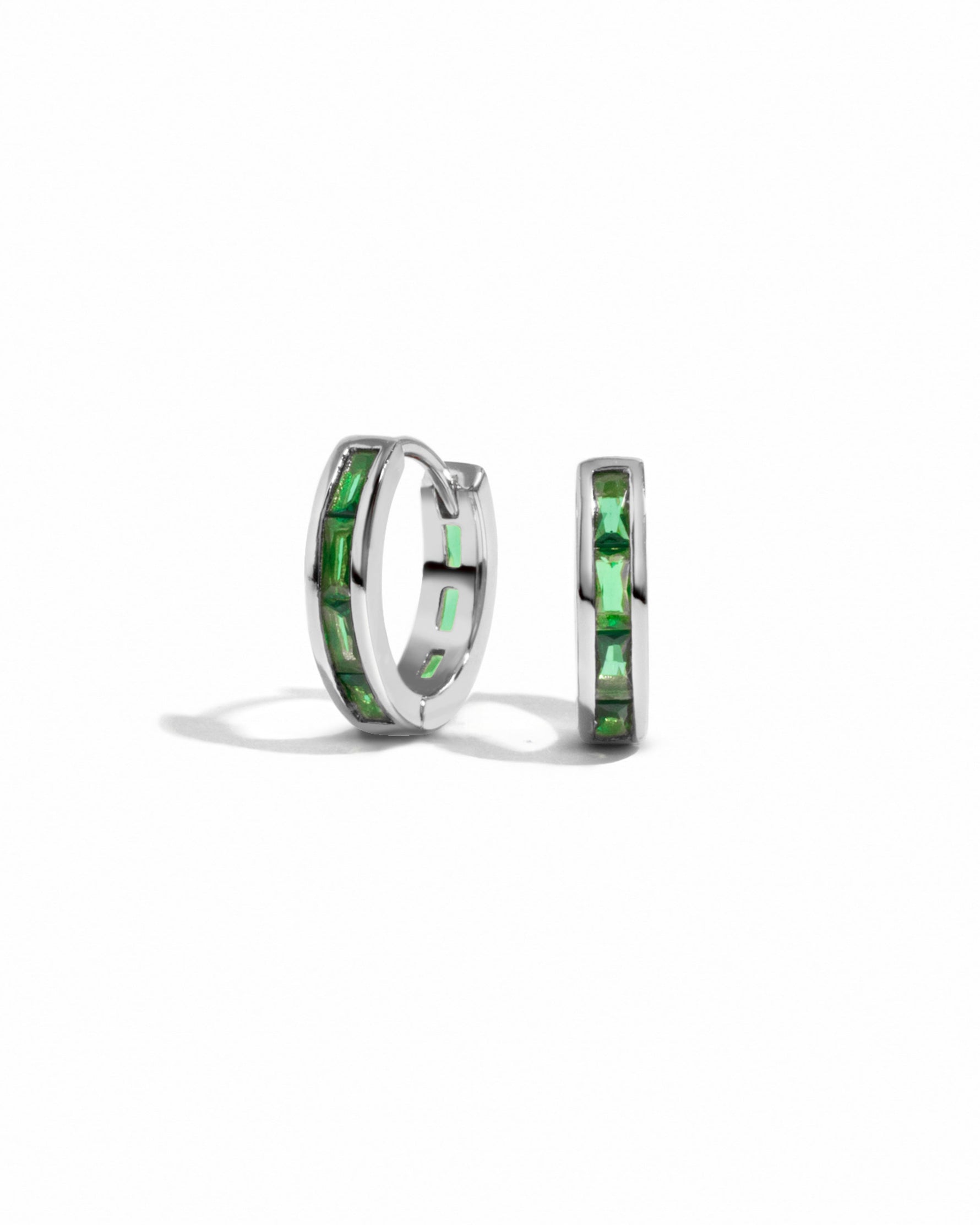 Sterling silver emerald huggie earrings on a white background