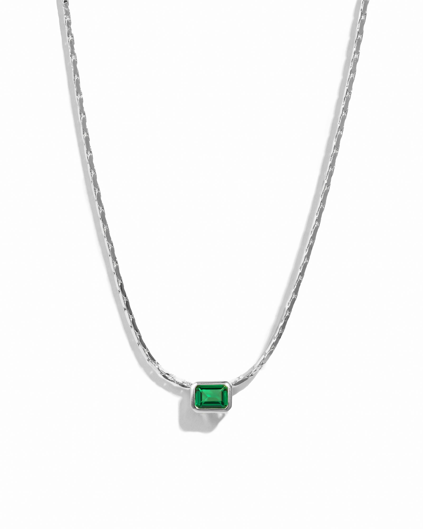 Silver chain necklace with a green gemstone pendant on a white background