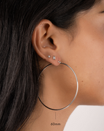 model wearing 60mm silver large hoop earrings, a small silver baguette stud, and a small bezel stud earring