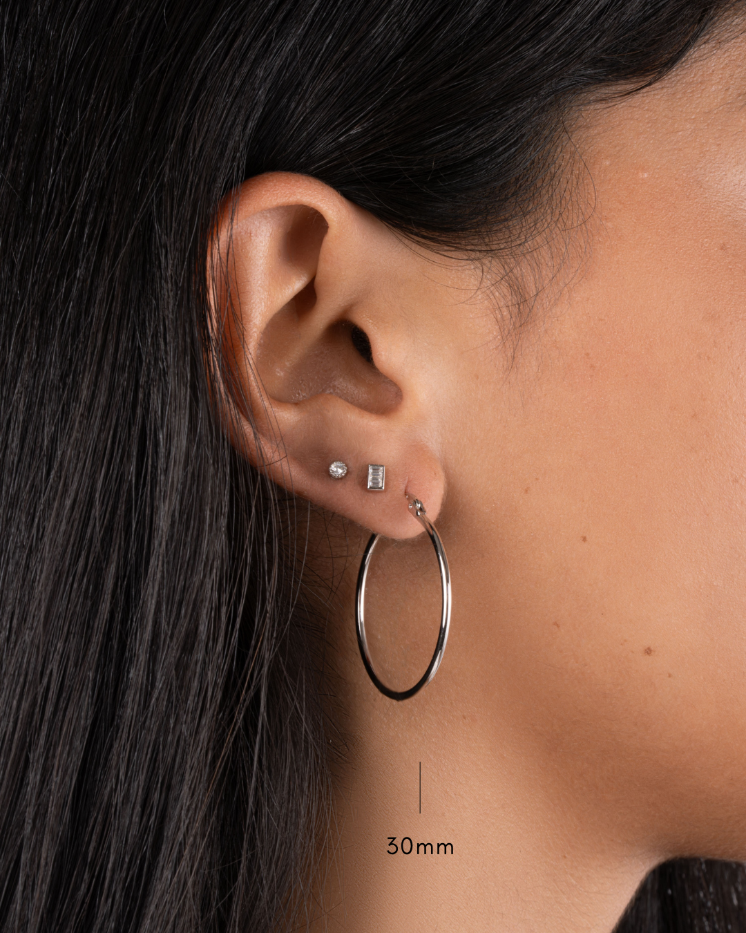 model wearing silver hoop earrings, a tiny stud earring and a tiny bezel stud earring