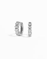 Pair of silver huggie hoop earrings with white cubic zirconia gemstones on a white background