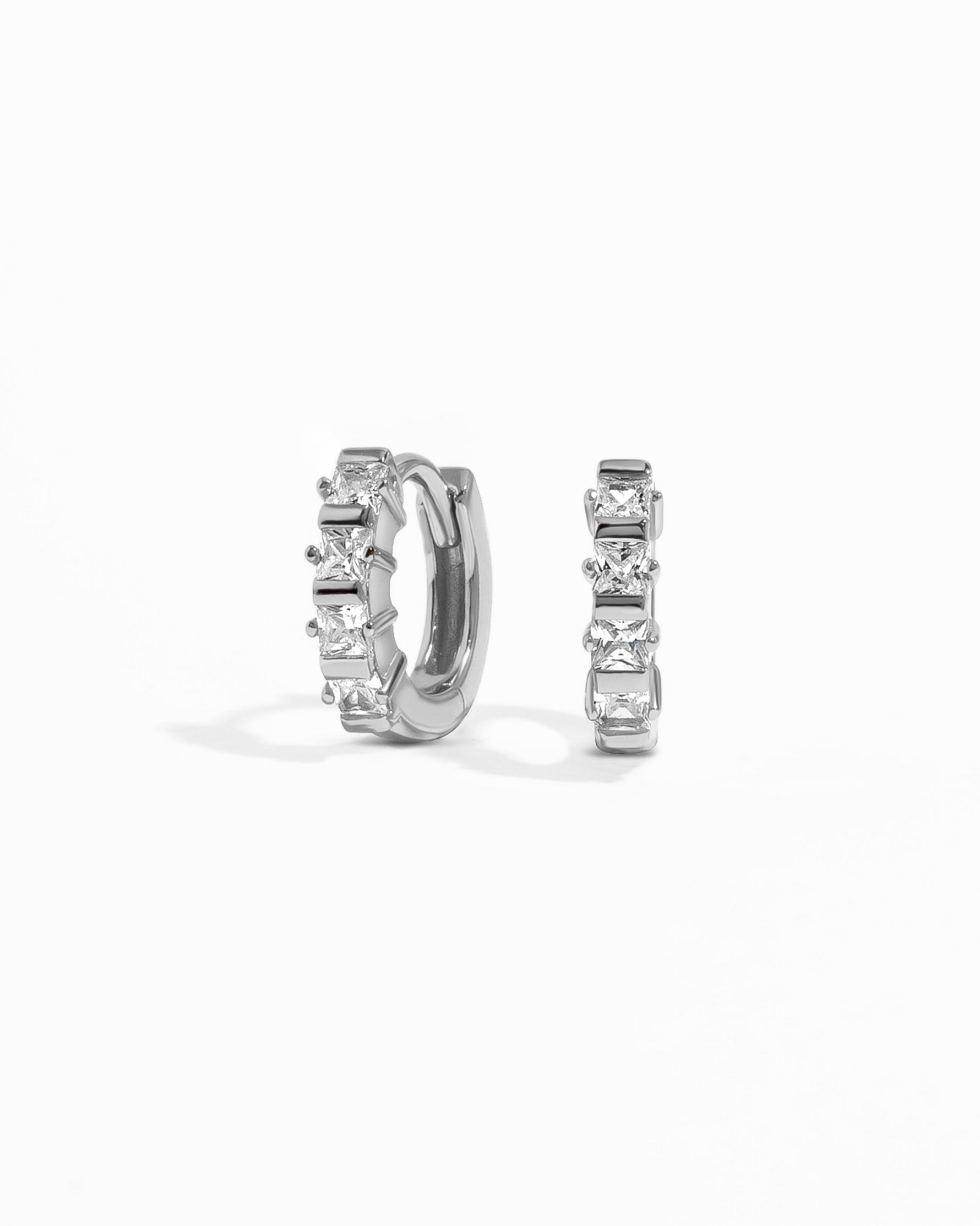 Pair of silver huggie hoop earrings with white cubic zirconia gemstones on a white background