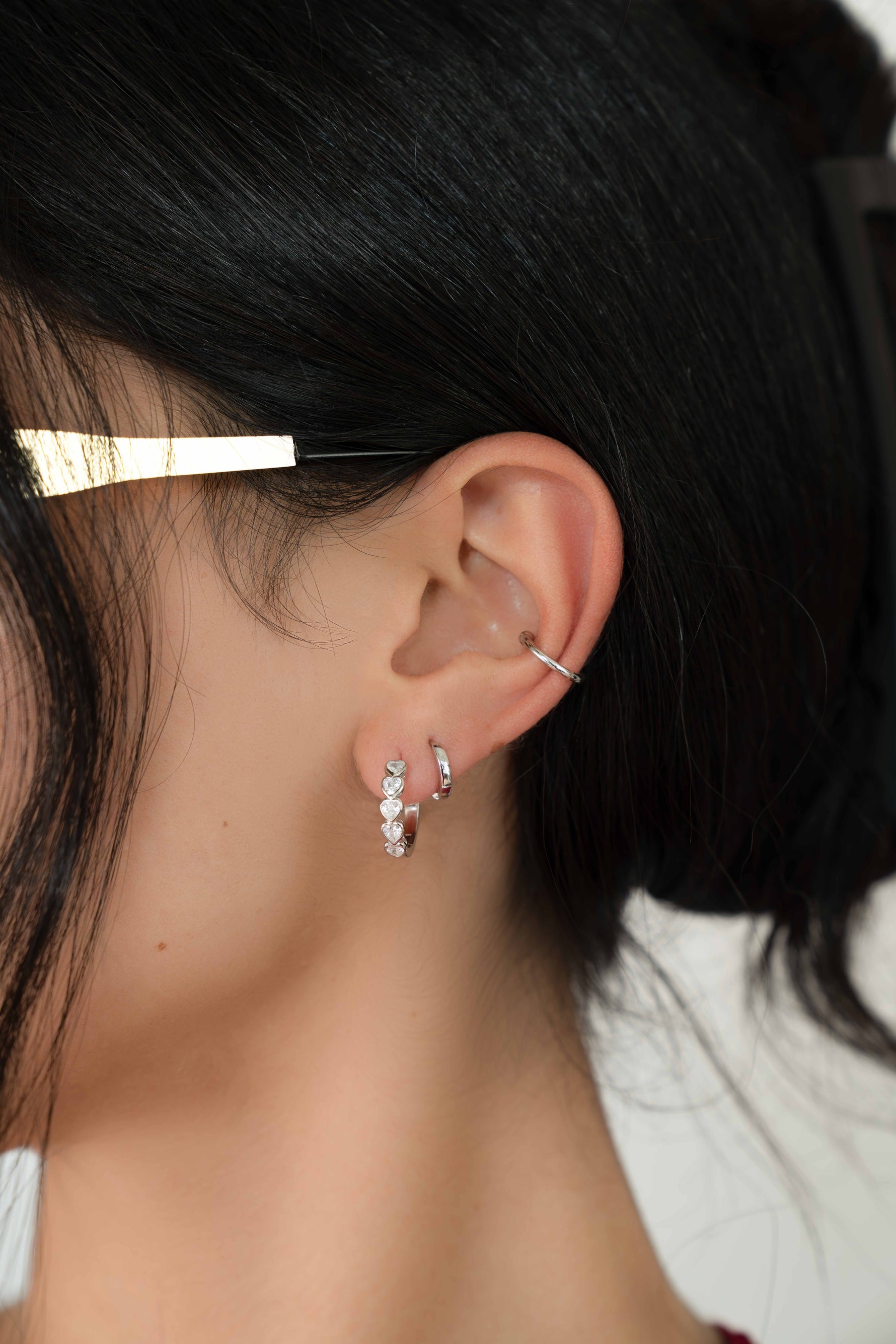 Silver huggies on model featuring heart huggie hoops, and a minimalist huggie hoop, with a simple ear cuff 
