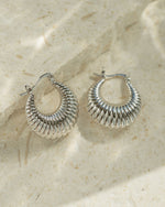 Vintage jewelry featuring silver hoop earrings on a textured beige surface