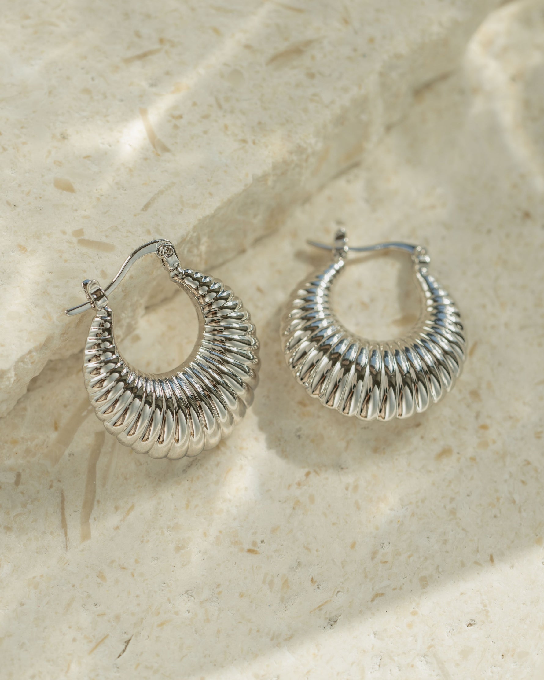 Vintage jewelry featuring silver hoop earrings on a textured beige surface