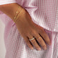 model wearing gold jewelry featuring an opal eternity ring, a pink cushion ring, and  dainty gold chain bracelets