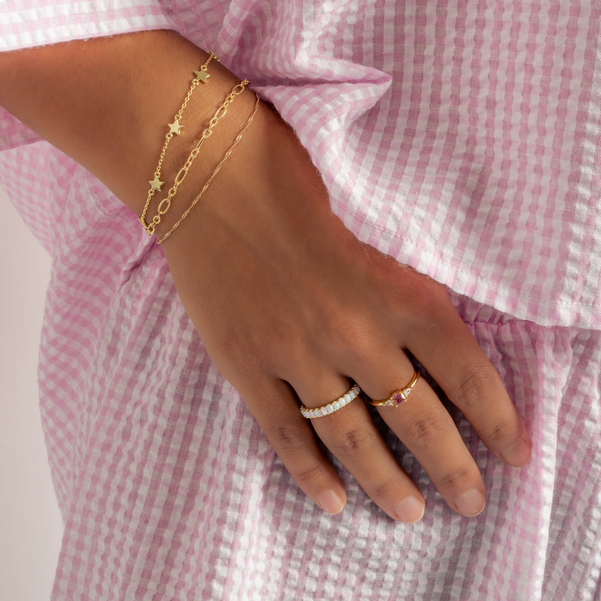 model wearing gold jewelry featuring an opal eternity ring, a pink cushion ring, and  dainty gold chain bracelets