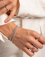 Close-up of hands on model wearing pave diamond bracelets and stackable silver rings featuring a bezel set baguette ring  