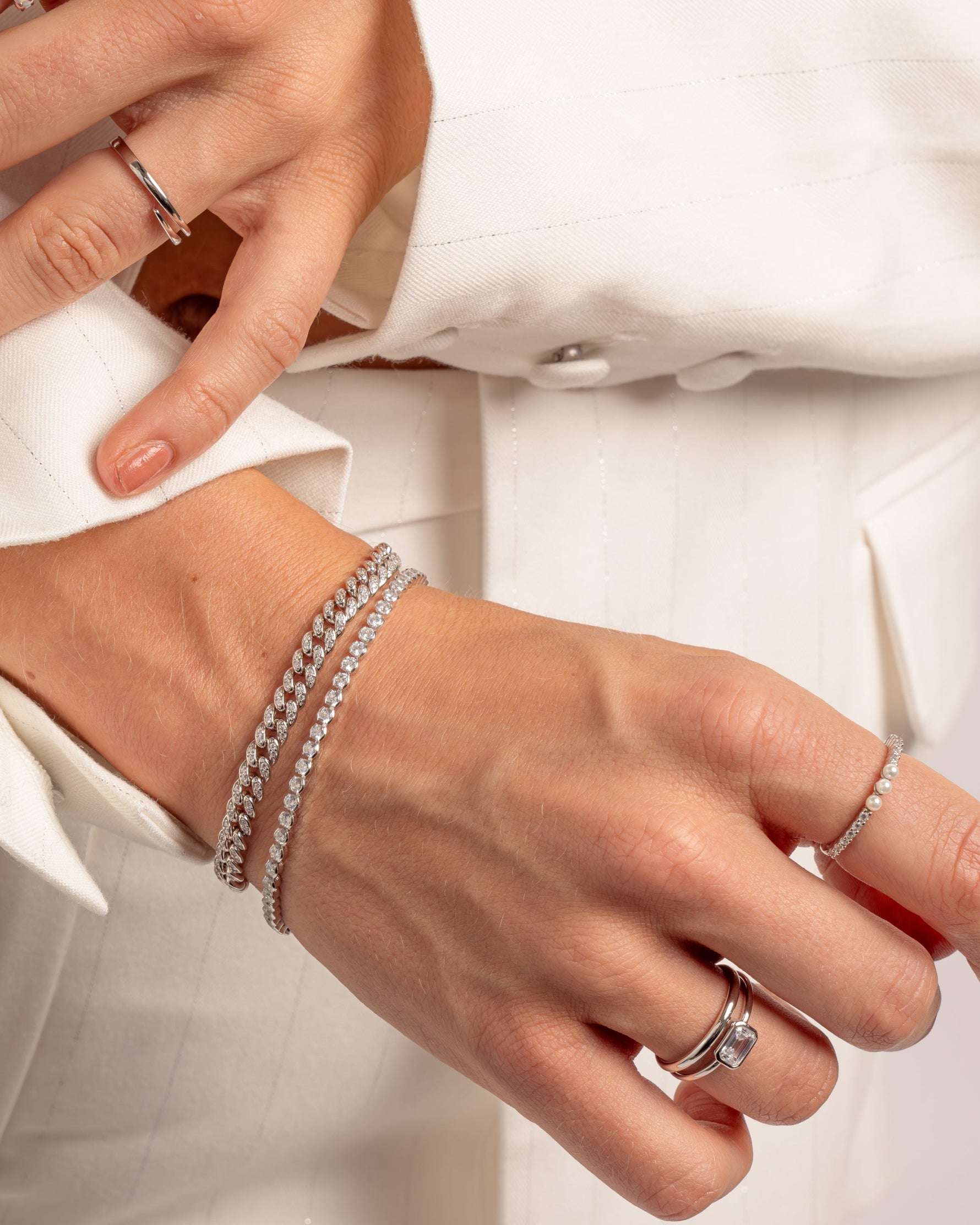 Close-up of hands on model wearing pave diamond bracelets and stackable silver rings featuring a bezel set baguette ring  