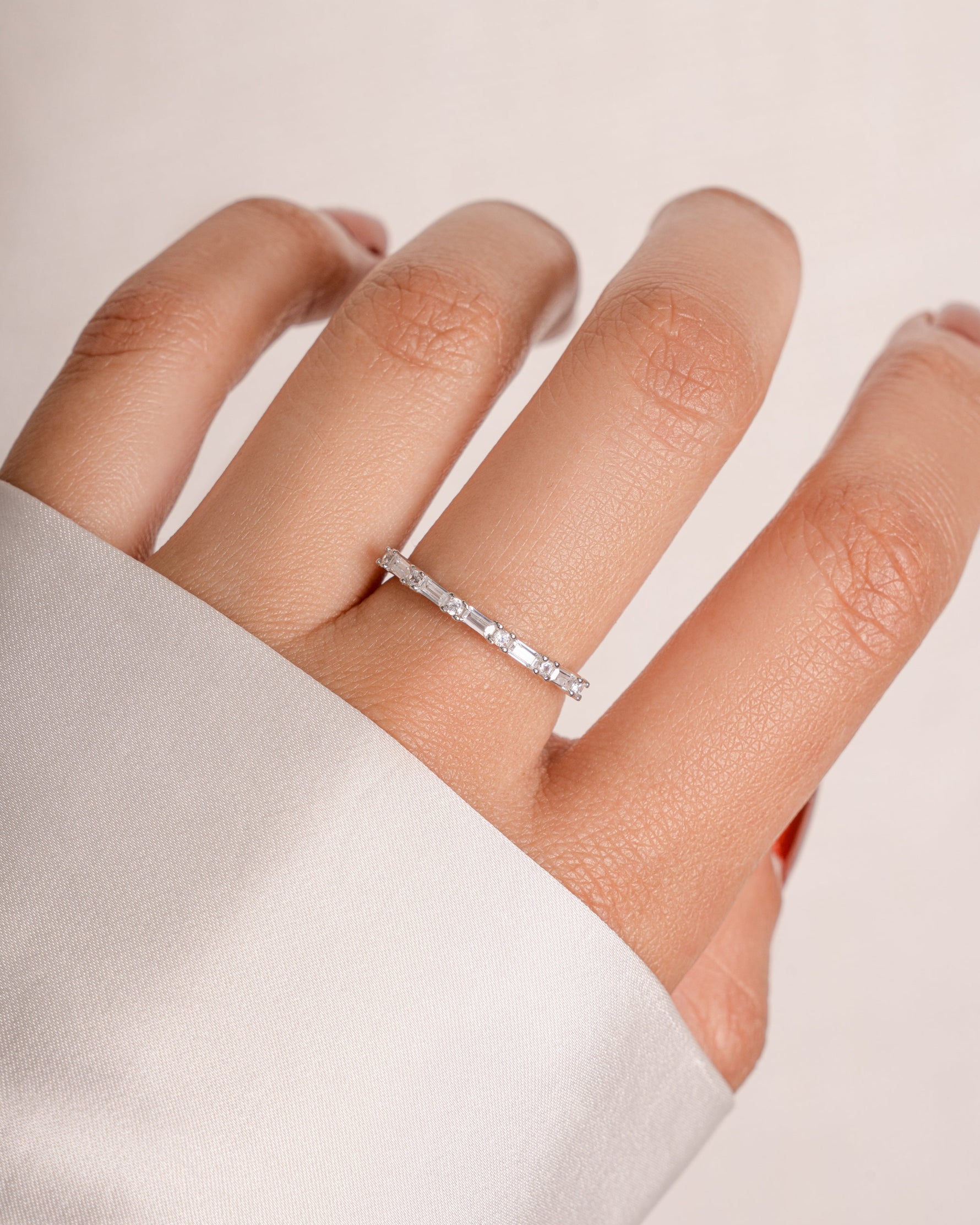 Hand wearing a sterling silver baguette ring on a plain background
