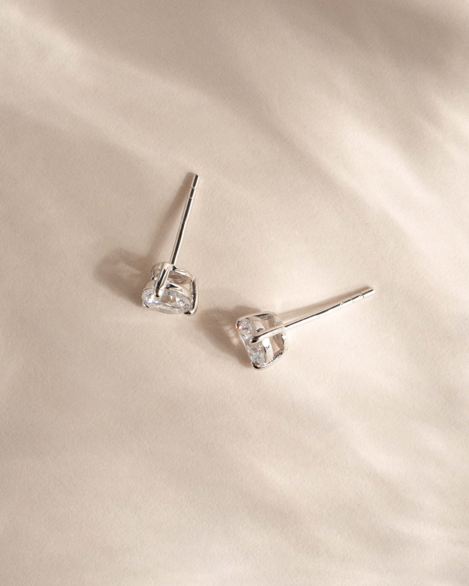 Pair of silver diamond stud earrings on a beige fabric background