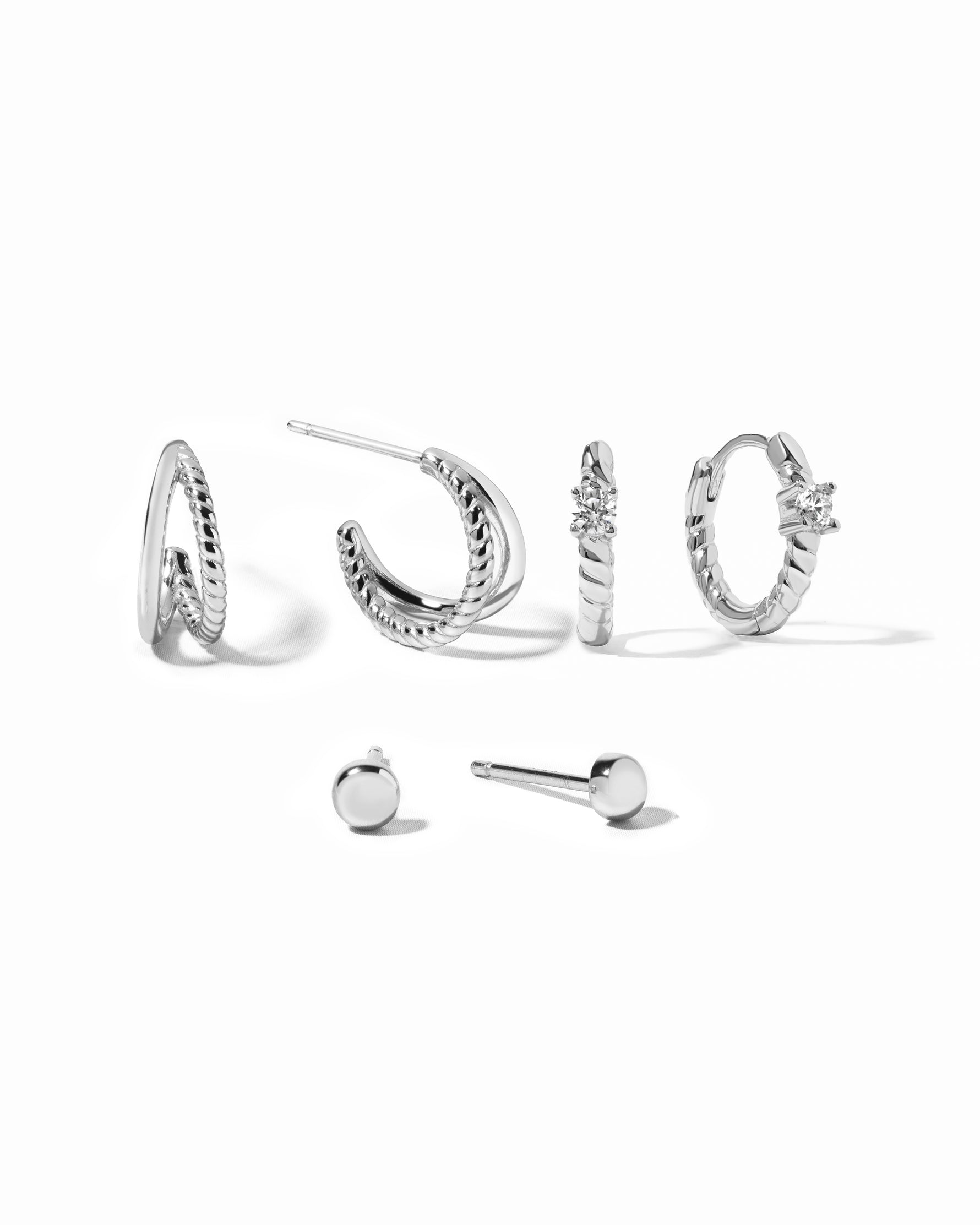 Set of silver hoop earrings with textured hoop earrings, spiral huggies, and stud earrings on a white background