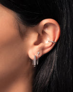 Close-up of a model ear wearing a silver spiral ear cuff, a diamond chain stud earring, and a square hoop earring