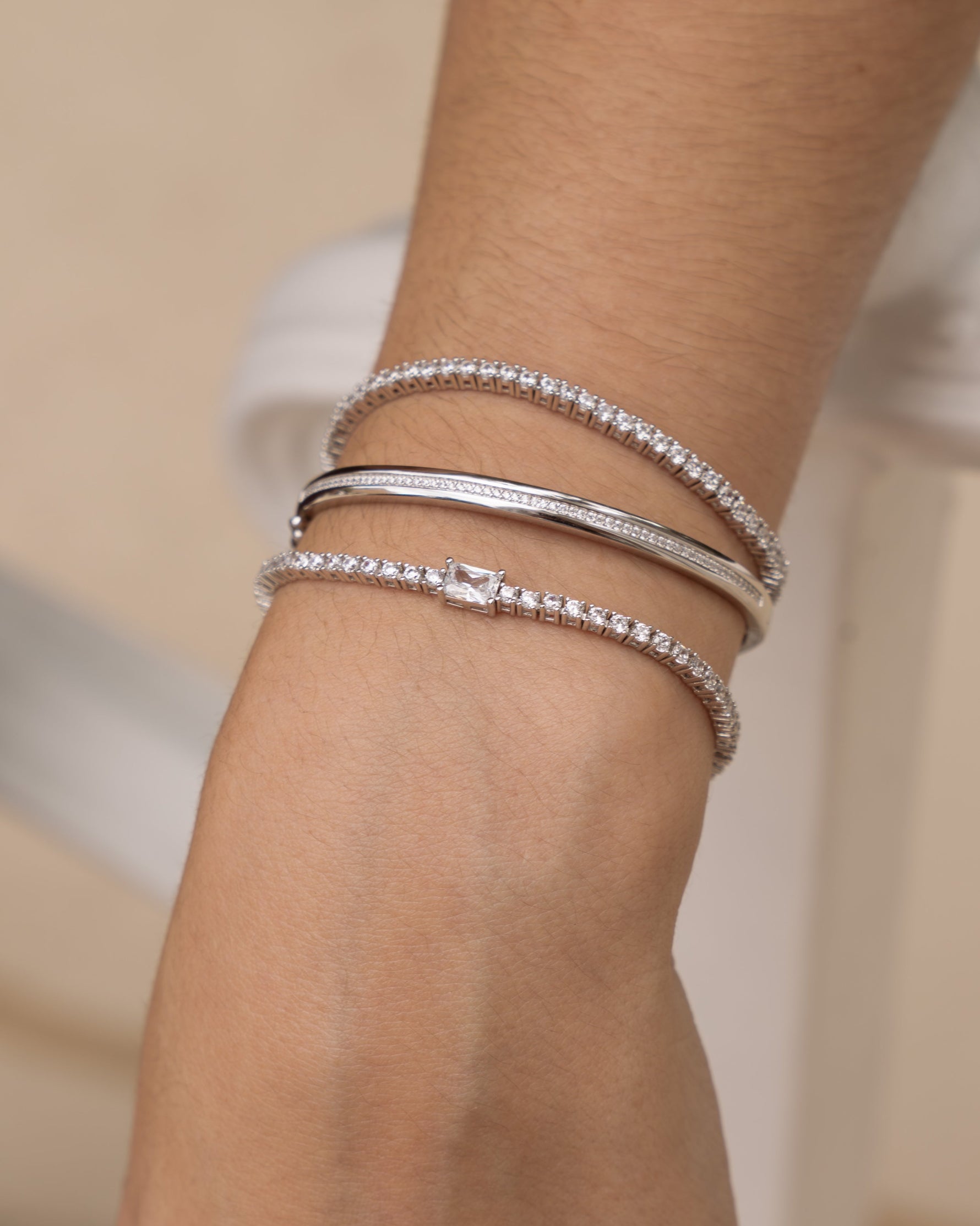 Model wearing sterling silver bracelet stack featuring two silver diamond tennis bracelets and a diamond bangle bracelet