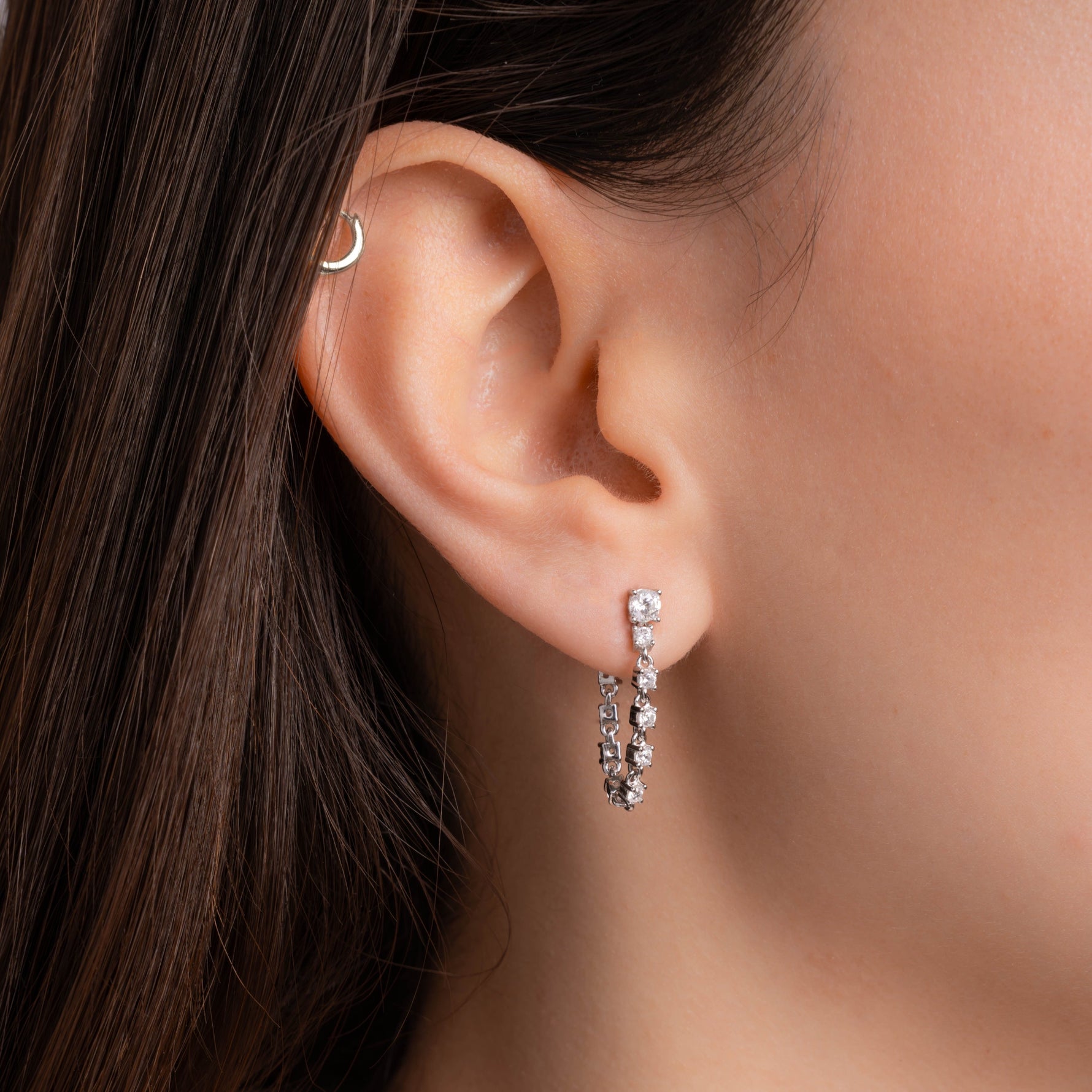 Model wearing tennis chain dangle earrings with diamond gemstones, set in silver. 
