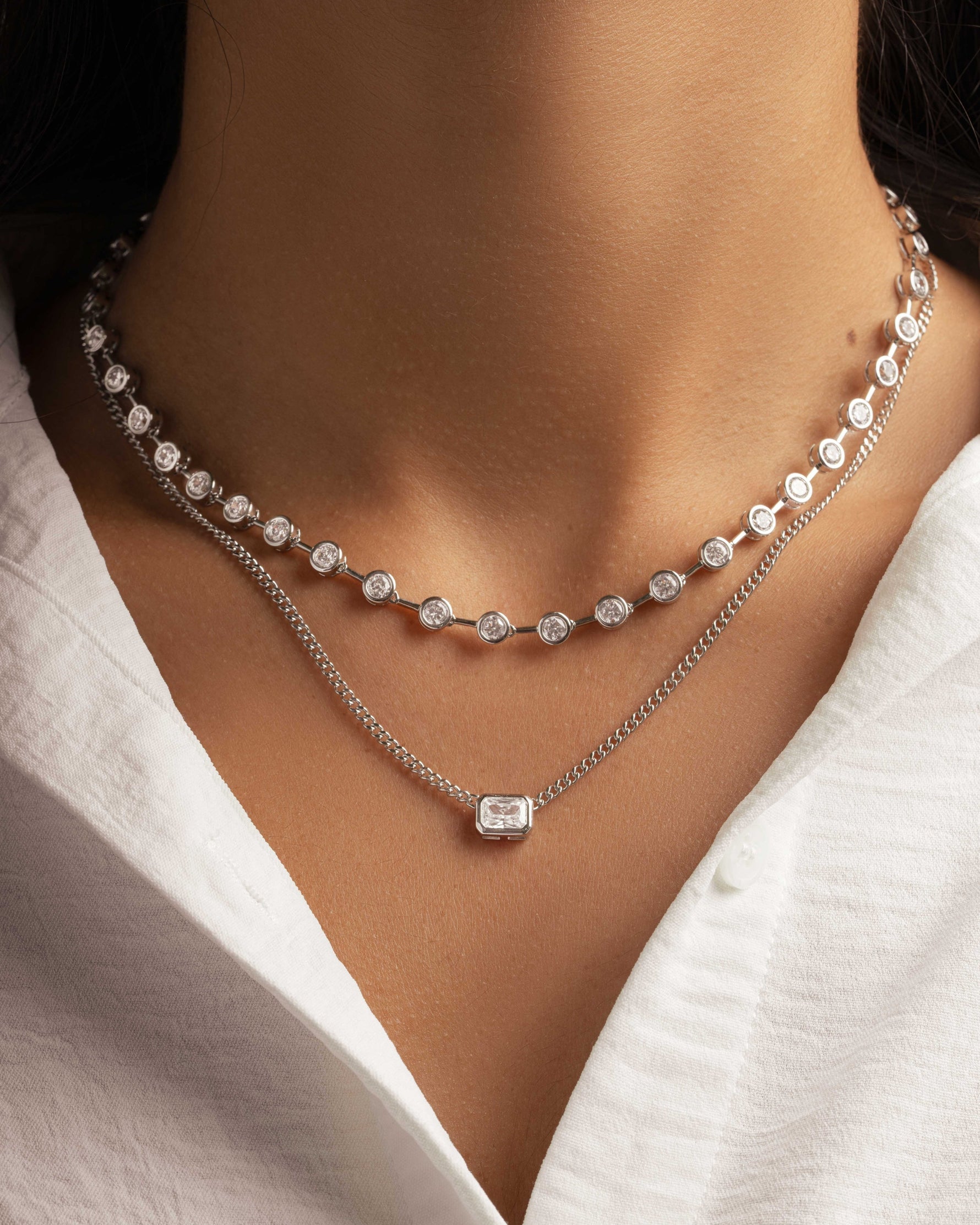 Model wearing diamond pendant necklace styled with a silver layering diamond tennis necklace 