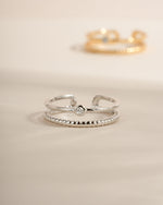 A sterling silver minimalist toe ring with a cubic zirconia bezel set stone and a blurred dainty ring in the background